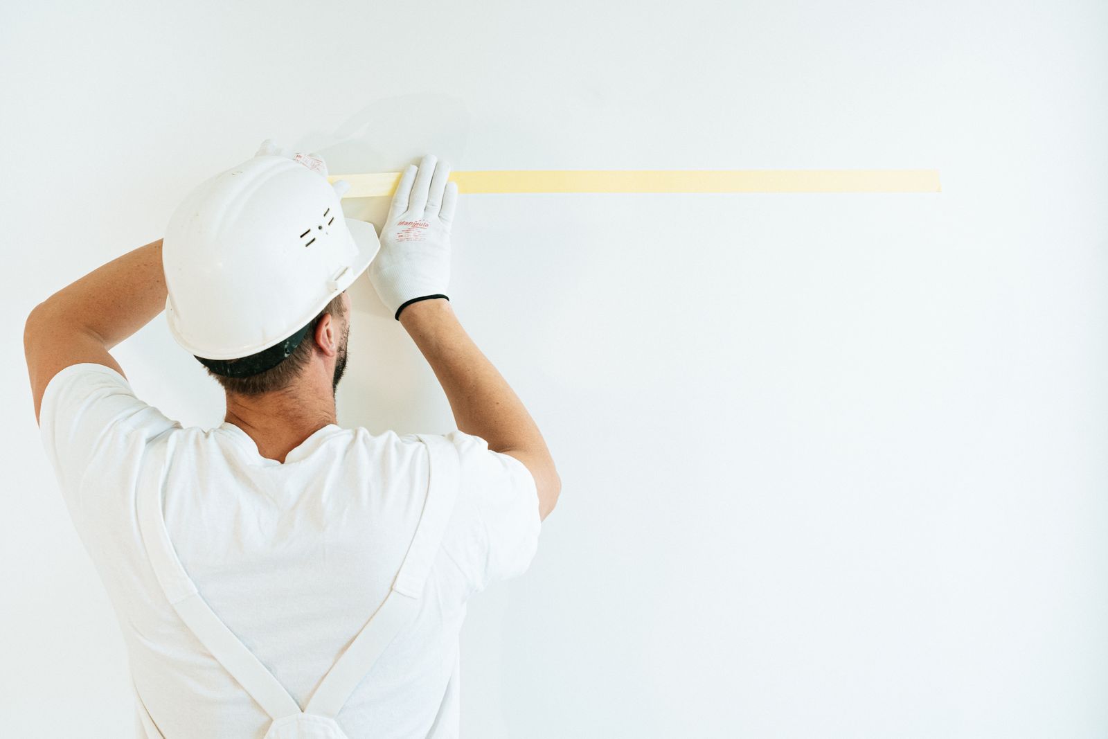 Maler klebt vor dem Streichen die Kanten einer Wand mit Malerband ab